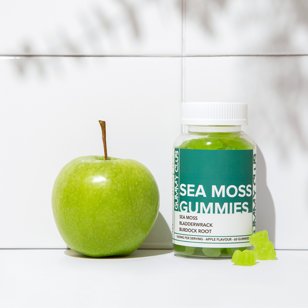 Bottle of Sea Moss Gummies next to a green apple on a white surface
